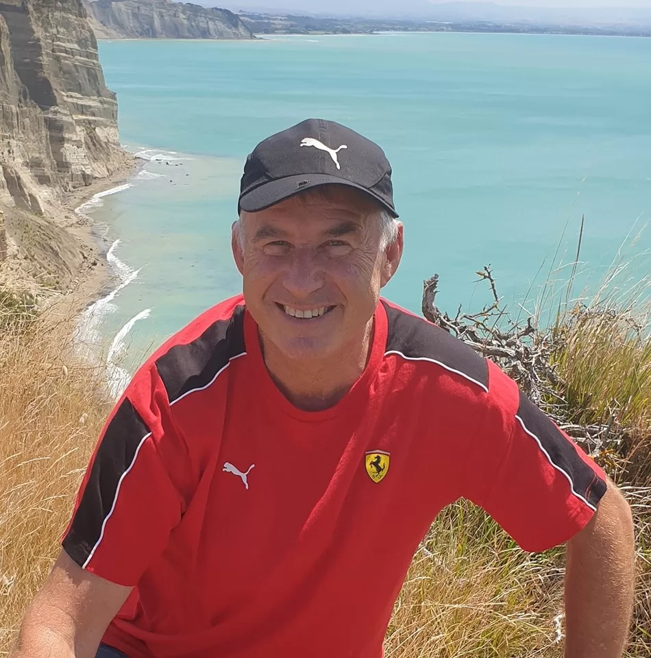 grant-image-red a man in a red shirt and black hat sitting on a cliff overlooking a body of water